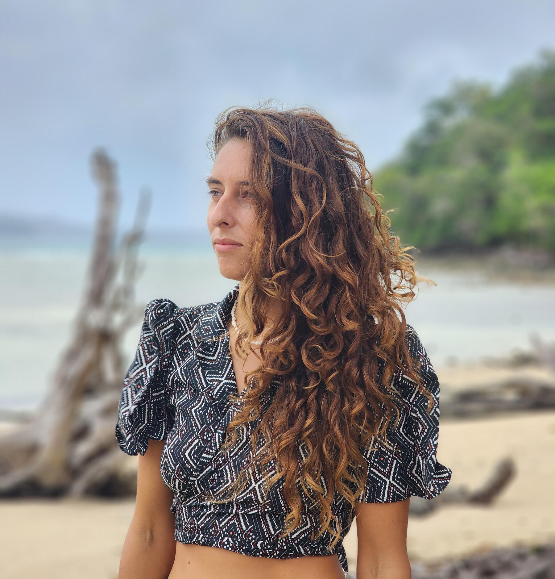 Samara Ruighaver, Breathwork Facilitator in Berlin and Breda Samara Ruighaver, founder of Inner Shift Wellness Coaching, standing on a quiet beach with curly hair, looking calmly into the distance.